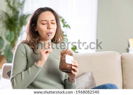 Young woman eating chocolate from a jar at home
