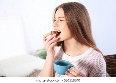 Young woman eating cookie with coffee in living room