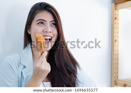 Young woman eating deep fried chicken. Asian woman holding fried chicken with copy space. Girl holding fried chicken drumstick. Bad food of health concept.