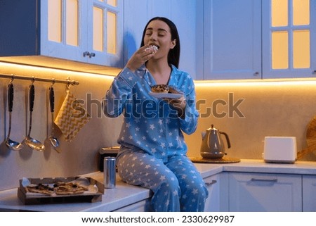 Young woman eating donut in kitchen at night. Bad habit