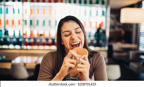 Young Woman Eating Fatty Hamburger.Craving Fast Food.Enjoying Guilty Pleasure,eating Junk Food.Satisfied Expression.Breaking Diet Rules,giving Up Diet.Unhealthy Imbalanced Nutrition Calorie Intake.