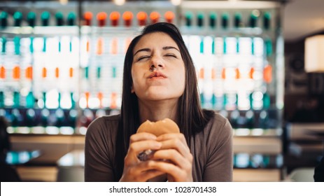 Young Woman Eating Fatty Hamburger.Craving Fast Food.Enjoying Guilty Pleasure,eating Junk Food.Satisfied Expression.Breaking Diet Rules,giving Up Diet.Unhealthy Imbalanced Nutrition Calorie Intake.