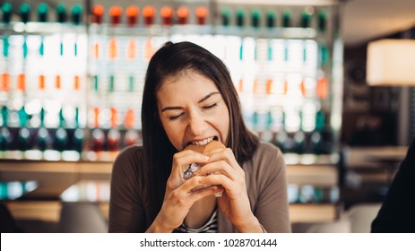 Young woman eating fatty hamburger.Craving fast food.Enjoying guilty pleasure,eating junk food.Satisfied expression.Breaking diet rules,giving up diet.Unhealthy imbalanced nutrition calorie intake.