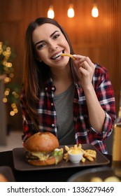 Young Woman Eating French Fries And Tasty Burger In Cafe