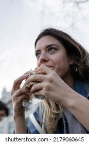 Young Woman Eating Grilled Fish Sandwich. The Focus Is On Her Hand. Low Angle Photograph. 