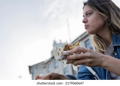 Young Woman Eating Grilled Fish Sandwich. The Focus Is On Her Hand. Low Angle Photograph. 