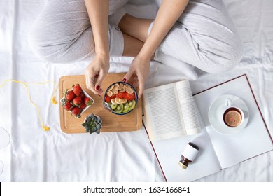 Young Woman Eating Healthy Breakfast In Bed. She Eaten From A Fully Bowl Cornflakes And Fruit. Top View On Bed