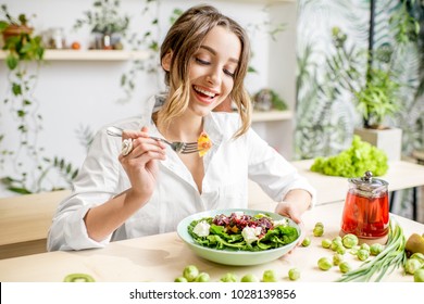 Young woman eating healthy food sitting in the beautiful interior with green flowers on the background - Powered by Shutterstock