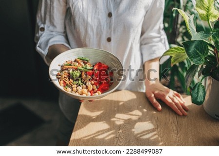 Young woman eating healthy food sitting in the beautiful interior with green flowers on the background