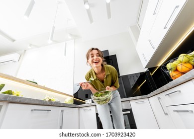 Young Woman Eating Healthy Salad On The Kitchen At Home, Wide Angle View On The Modern White Interior