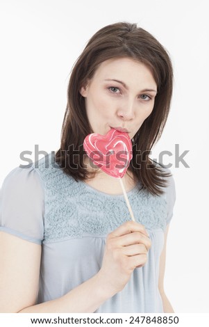Young woman eating heart shaped lollipop, portrait