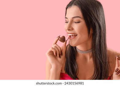 Young woman eating heart-shaped chocolate candy on pink background, closeup - Powered by Shutterstock