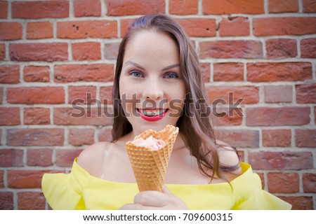 Young woman eating ice cream outdoor in street, red brock wall background