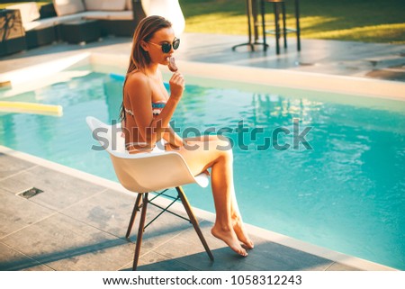 Young woman eating icecream near the swimming pool at hott summer day