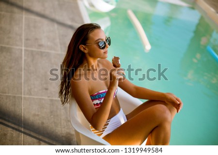 Young woman eating icecream near the swimming pool at hot summer day
