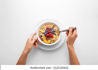 Young Woman Eating Muesli Cereal Breakfast With Berry Fruit In A White Bowl Viewed Directly From Above. Female Hand Holding A Spoon With Fresh Rich In Fiber Granola Dish Viewed From Above. Top View.