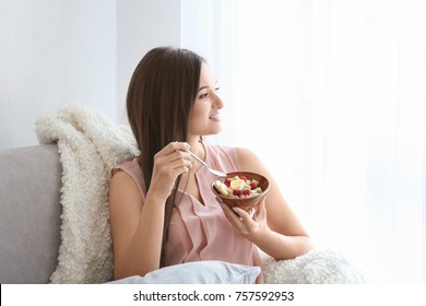 Young Woman Eating Oatmeal On Sofa At Home