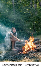 Young Woman Eating Roasted Marshmallows While Camping Near The Lake. Woman Roasting Marshmallows Near Bonfire. Young Woman Having A Camping