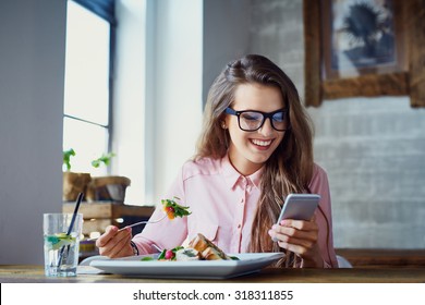 Young woman eating salad at restaurant and texting on smartphone - Shutterstock ID 318311855
