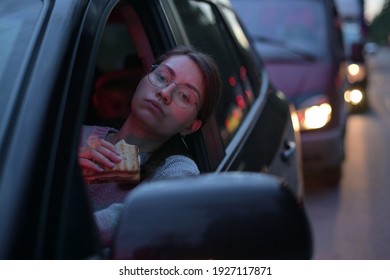 Young Woman Eating A Sandwich While Standing In A Traffic Jam. Food On The Go, Rush Hour