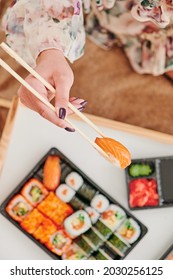 Young Woman Eating Sushi At Home. Home Food Delivery Concept. Japan Food. Top View. Space For Text