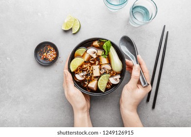 Young Woman Eating Tasty Asian Vegetarian Or Vegan Soup Served In Black Bowl On Grey Table. View From Above. Horizontal. 