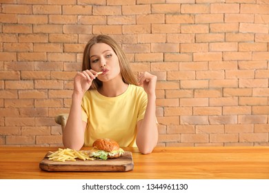 Young Woman Eating Tasty Burger With French Fries At Table