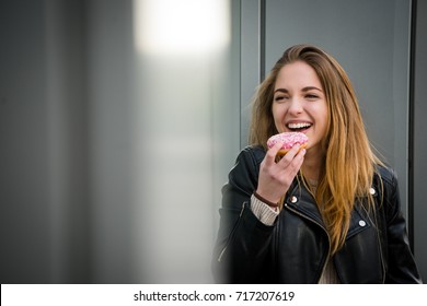 Young Woman Eating Tasty Donut Outdoor At Shop Window