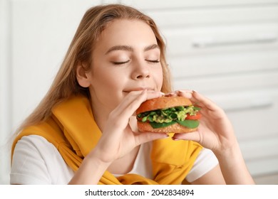 Young Woman Eating Tasty Vegan Burger In Kitchen