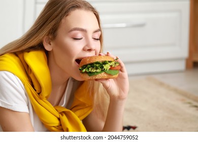 Young Woman Eating Tasty Vegan Burger In Kitchen