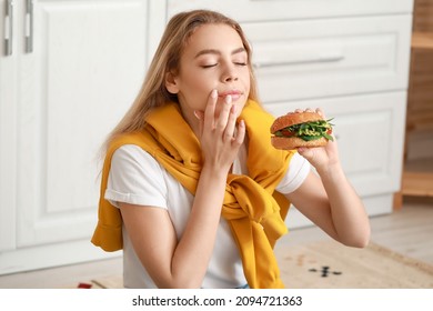 Young Woman Eating Tasty Vegan Burger In Kitchen