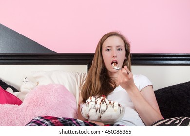 A Young Woman Eats A Giant Ice Cream Sundae While Sitting In Bed