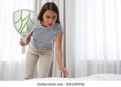 Young Woman With Electric Fly Swatter In Bedroom. Insect Killer