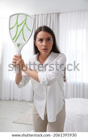 Young woman with electric fly swatter indoors. Insect killer