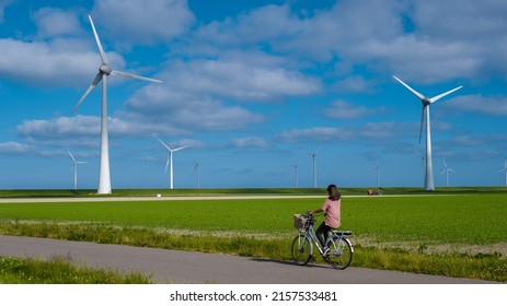 young woman electric green bike bicycle by windmill farm, windmills isolated on a beautiful bright day Netherlands Flevoland Noordoostpolder