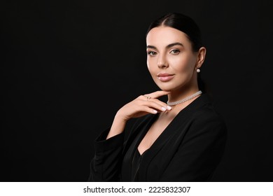 Young woman with elegant pearl jewelry on black background, space for text