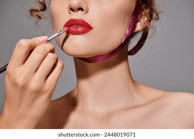 A young woman elegantly applying lipstick to her lips in a studio setting, showcasing classic beauty. - Powered by Shutterstock