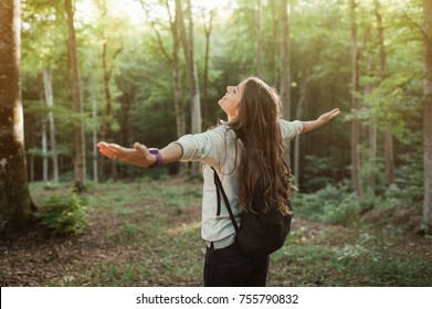 Young woman emgracing the sun and nature with backpack in the forest on sunset light in the autumn season, looking up, exploring the nature.
