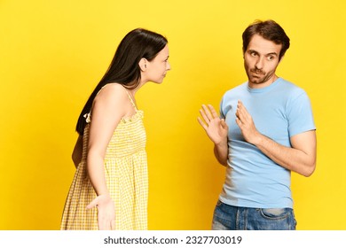 Young woman emotionally talkin to man, asking questions against yellow studio background. Man making excuses. Concept of friendship, relationship, communication, emotions, lifestyle, ad