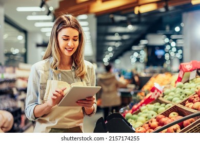 Young woman, employee with apron holding digital tablet and checking condition of product in the store - Shutterstock ID 2157174255