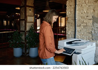 Young woman employee working on printer at coworking office