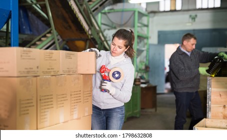 Young Woman Engaged In Family Production Of Olive Oil, Sealing Carton Boxes With Sticky Tape Dispenser At Warehouse