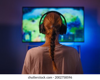 A young woman is engaged in gaming. Plays video games. The woman is wearing headphones. In front of her is a computer. Close-up. Shooting from the back. - Shutterstock ID 2002758596