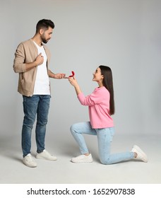 Young woman with engagement ring making marriage proposal to her boyfriend on light grey background