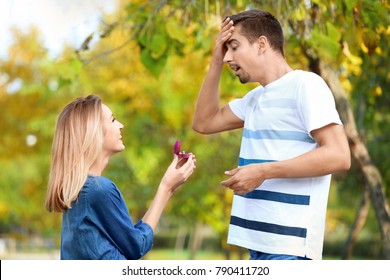 Young woman with engagement ring making proposal of marriage to her boyfriend in park