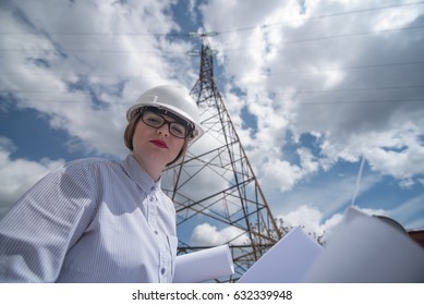 Young Woman Engeneer With Electicity Grid Plans And Power Lines In Background