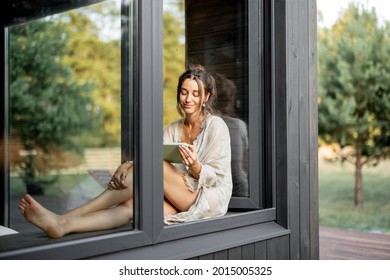 Young Woman Enjoy Of Resting At Modern House Or Hotel In Pine Forest, Sitting With Tablet On The Window Sill. Concept Of Solitude And Recreation On Nature. Beautiful Destinations For Vacation