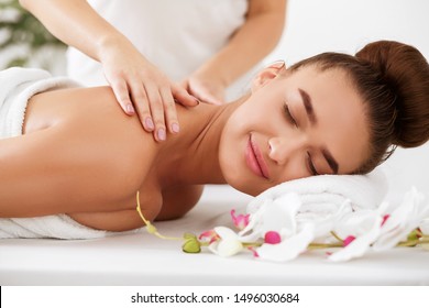 Young woman enjoying back massage in spa salon with orchid flowers nearby