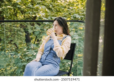 Young woman enjoying a calm morning on the balcony with a glass of juice, morning rituals, relaxation, peaceful start to the day, nature view. - Powered by Shutterstock