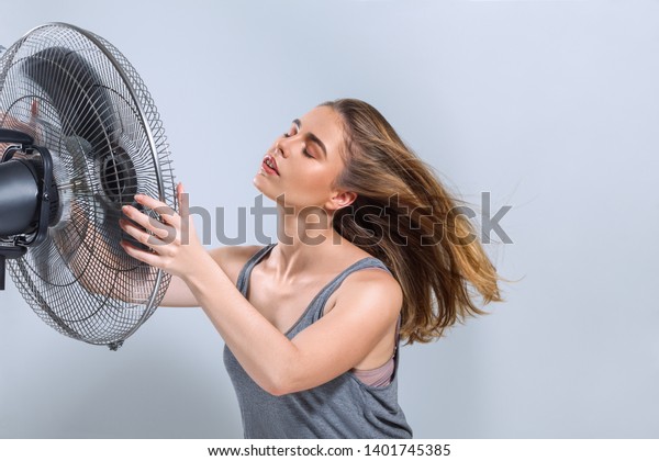 暑い夏の熱波で扇風機から冷たい風を受ける若い女性 の写真素材 今すぐ編集
